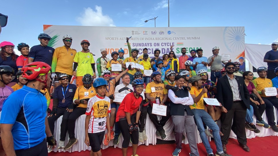 A group of cyclists standing on a stage with World Bicycle Day branding in the backdrop.